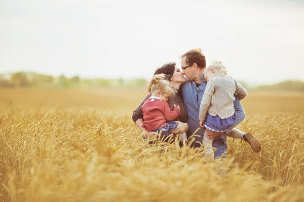 Mother and father holds on a hands their little children and kiss each other on a field — Stock Photo, Image