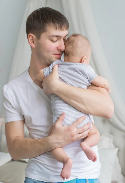 Jovem pai segura as mãos de seu bebê em casa (visão traseira ) — Fotografia de Stock
