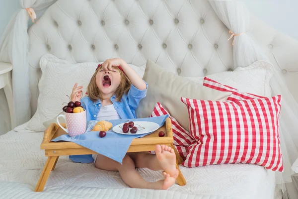 Cute little girl eats a cherry at breakfast on a bed