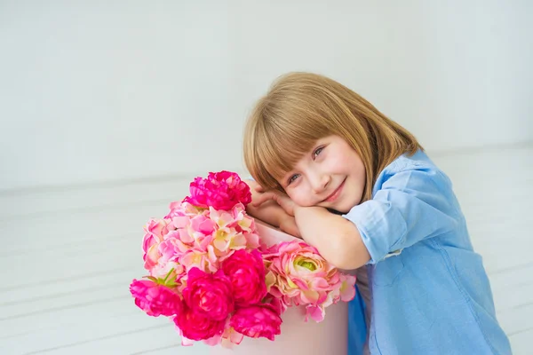 Το μικρό κορίτσι που κάθεται σε ένα πάτωμα κοντά σε ένα κουτί με ένα λουλούδια και χαμογελαστός — Φωτογραφία Αρχείου