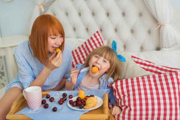 Madre e figlia piccola divertente mangiare a colazione su un letto — Foto Stock