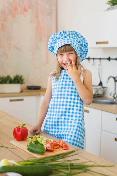 Ritratto di bambina in abiti da cuoca sorride dietro un tavolo su una cucina — Foto Stock