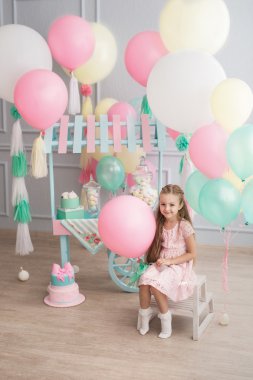 Küçük kız oturur bir odada renkli baloons dekore edilmiştir.