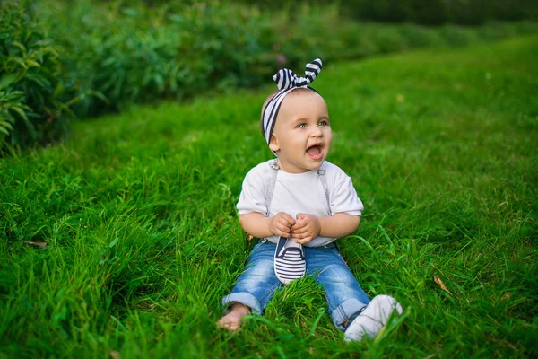 Ένα μωράκι με ένα τζιν ρούχα που κάθεται σε ένα χόρτο — Φωτογραφία Αρχείου