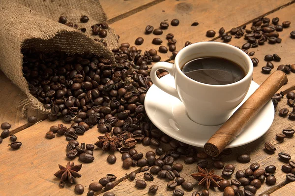 Kahve çekirdekleri, torbalama ve ahşap puro ile kahve fincanı.