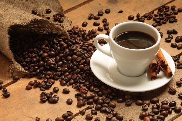 Kahve fincanı kahve çekirdekleri, torbalama ve ahşap üzerine tarçın ile.
