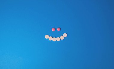 Gülen yüz mavi arka planda beyaz ve pembe haplarla kaplıdır. Sağlığınıza. Keyfin yerinde.