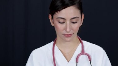 Kadın doktor elinde şırıngayla dışarı sıvı fışkırtıyor. Kameraya karanlık arka planda bakıyor..