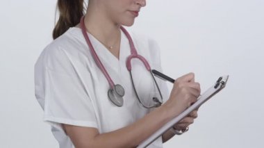 Hemşire panoya yazı yazıp kameraya bakarken başını sallıyor..