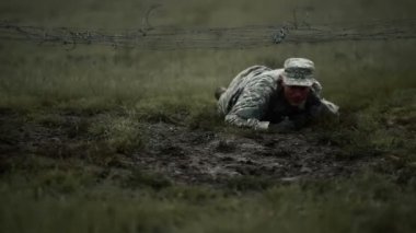 Alçak dikenli tellerin altında sürünen asker