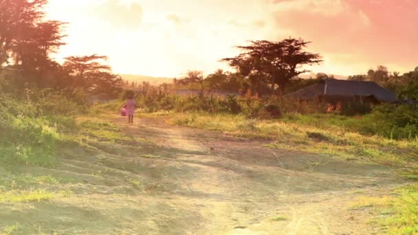 Niña en vestido rosa corre a lo largo de camino de tierra en África . — Vídeo de stock