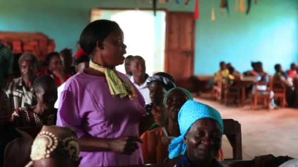 Uma mulher levanta-se, fala; outros sentam-se, ouvem durante a igreja no Quênia, África — Vídeo de Stock