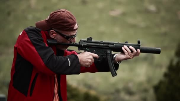 Man in baseball cap and red jacket shooting an MP5 — Stock Video