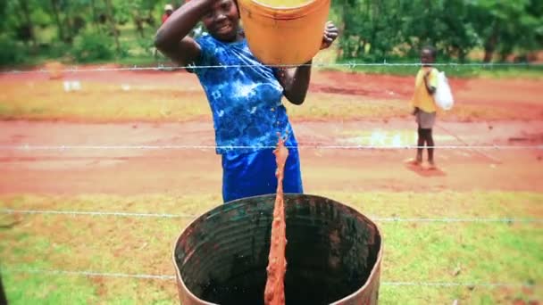 Een vrouw giet roodachtig water over een schutting in een vat in Kenia, Afrika — Stockvideo