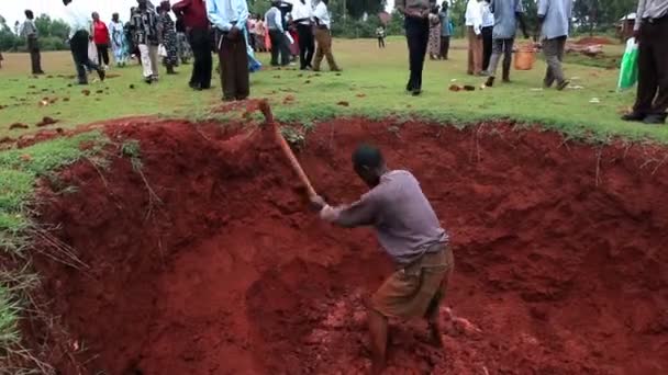 Een man graven in een diepe put; anderen kijken van bovenaf — Stockvideo