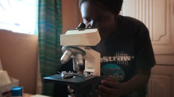 Uma mulher olha através de um microscópio dentro de uma clínica médica no Quênia, África — Vídeo de Stock