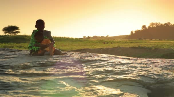 Jovem sentada em uma rocha com um bebê ao pôr do sol no Quênia . — Vídeo de Stock