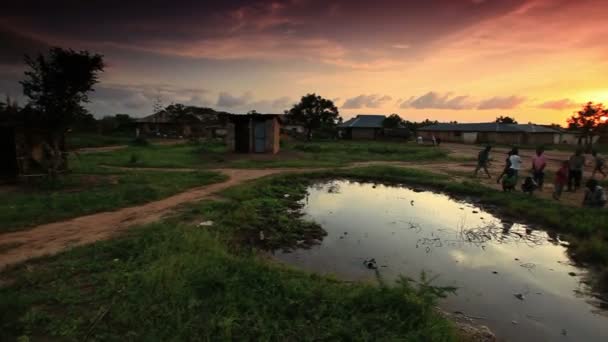 Jongens spelen op dorp water gat bij zonsondergang in Afrika. — Stockvideo