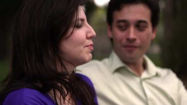 Un plano estático de una joven pareja riendo y bromeando juntos en un banco del parque . — Vídeo de stock