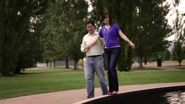 Et bilde av et par som går rundt en fontene sammen. – stockvideo