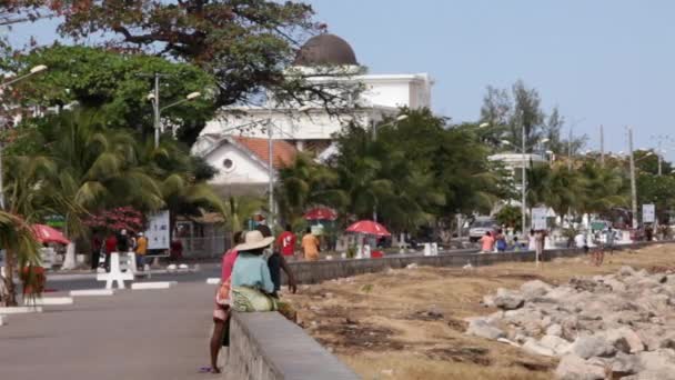 Personer som sitter längs trottoaren bredvid strandlinjen. — Stockvideo