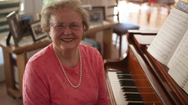 Un plano estático de una anciana feliz sentada en un banco de piano junto a un piano . — Vídeos de Stock