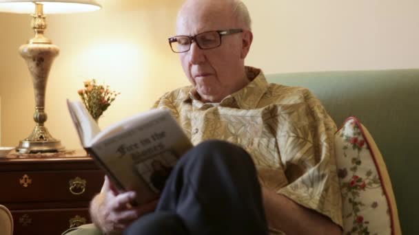 Eine statische Aufnahme eines älteren Mannes, der ein Buch auf einer Couch liest. — Stockvideo