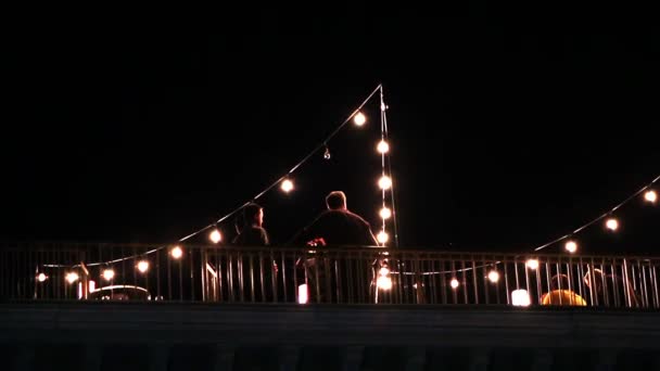 Vista de pessoas em um convés lá fora à noite com luzes penduradas ao redor . — Vídeo de Stock