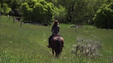 Slow motion shot of a woman riding horseback up a hill.