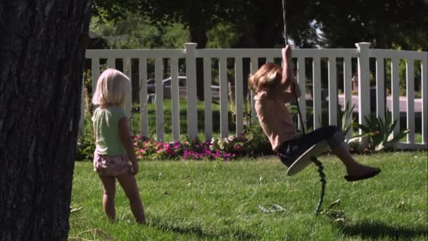 Niño balanceándose en un columpio de árbol mientras otro mira — Vídeos de Stock