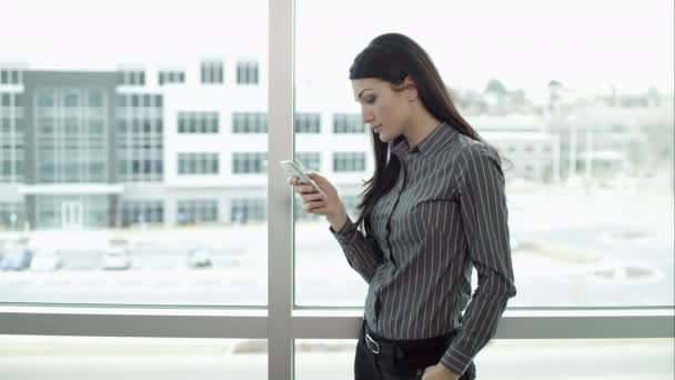 Mujer de pie junto a las ventanas usando smartphone . — Vídeo de stock