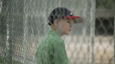 Sığınağın zincir bağlantı çit arkasında oturan çocuk.