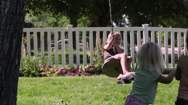 Zwei kleine Mädchen beobachten ein anderes beim Reiten einer Baumschaukel — Stockvideo