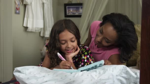 Slow motion pan of mother and daughter writing in book. — Stock Video