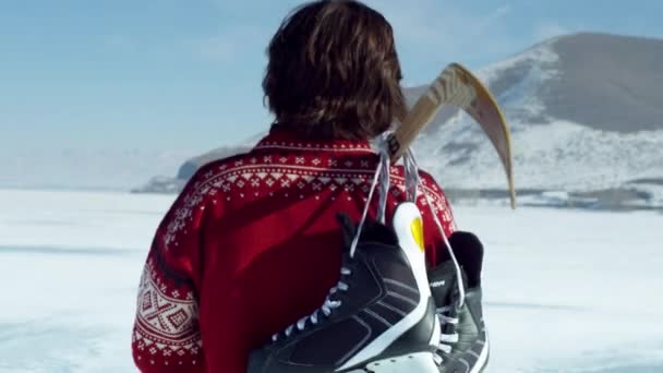 Boy walking through a snowy field with hockey gear. — Stock Video