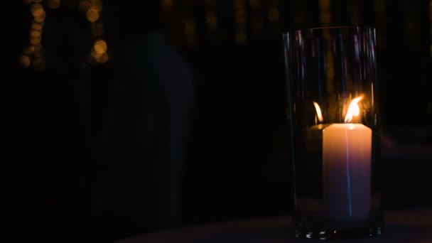 Grote witte kaars staande op een tabel onder een glazen kopje gevlamd terwijl er staan mensen op een achtergrond in een restaurant of een nachtclub. — Stockvideo