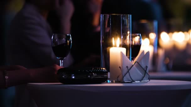 Imágenes de cerca de la mesa elegantemente decorada en el restaurante, mujer sosteniendo una copa de vino tinto, bolso de embrague negro de lujo está cerca. El hombre trae un plato con comida y tomar una copa . — Vídeos de Stock