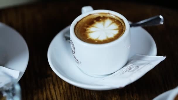 Primer plano del sabroso café servido en tazas blancas, una con forma de flor hecha de espuma con pegatinas de azúcar y cucharas de plata en platos pequeños . — Vídeos de Stock