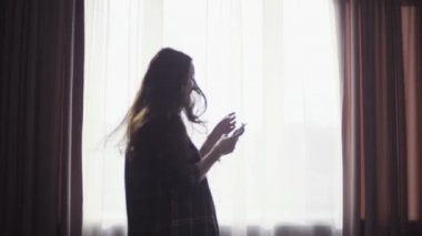 Enthusiastic happy girl listens to the music from smartphone in her hands, spins,  dances and makes fun,earphones plugged into the device.