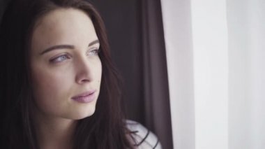 Close-up footage of female in her 20s looks at window and then change her gaze into camera.