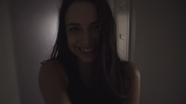 Joven mujer feliz atractiva corre a través de un pasillo en el apartamento y mirando a su alrededor, luego entra en un dormitorio y se sienta en una cama. tiro selfie . — Vídeos de Stock