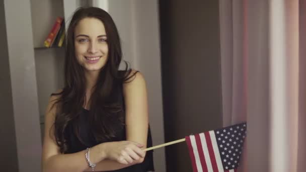 Lassított felvételeket egy lány áll a nappaliban, tesz egy ápolatlan mosoly és tartsuk lenyomva a zászló az Egyesült Államok. — Stock videók