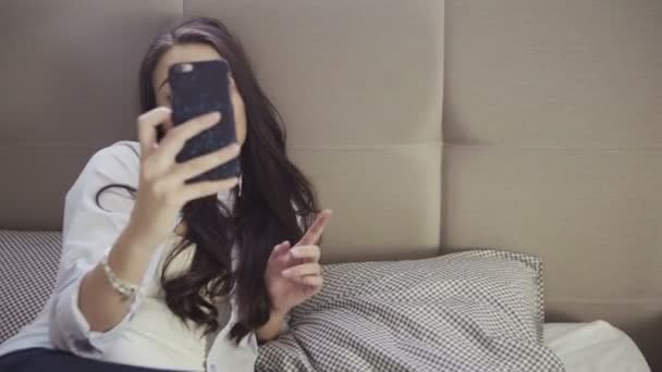 Joven hembra se encuentra en un sofá y hace expresiones divertidas para una selfie . — Vídeos de Stock