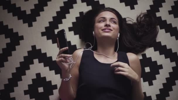 Повільні кадри молодої жінки, яка лежить на підлозі, слухає музику з підключеними навушниками . — стокове відео