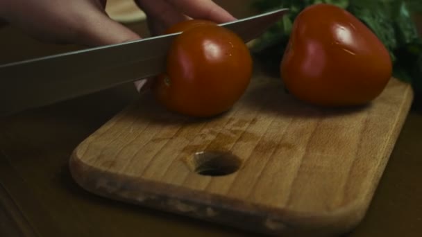 La mujer corta un tomate entero en dos rebanadas grandes en un plato de madera, imágenes de primer plano . — Vídeo de stock