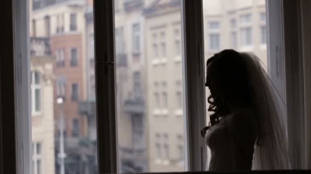 Young beautiful bride staying near the window and waiting for her groom at home. — Stock Video