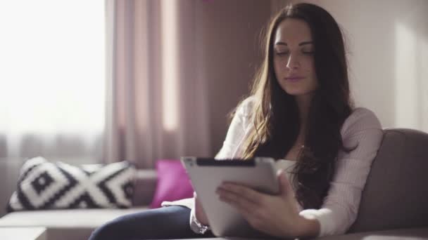 Szép nő, ő 20-as, a nappaliban ül, és a mobil eszköz segítségével. — Stock videók