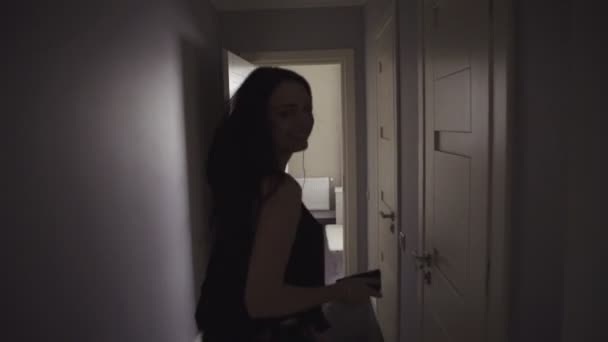 Slow motion footage of a young attractive happy woman who is running through a hall in apartment and looking around, girl listens to the music on her mobile device with earphones plugged-in. — Stock Video