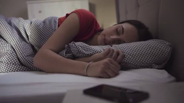 Gadis berambut cokelat yang tampan adalah bangun di tempat tidur dan mulai menggunakan perangkat mobile nya. — Stok Video