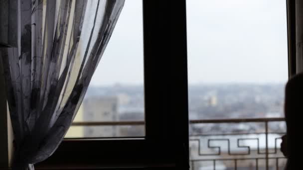 Attractive young lady having a rest and drinking a cup of tea or coffee in front of the window at home. — Stock Video